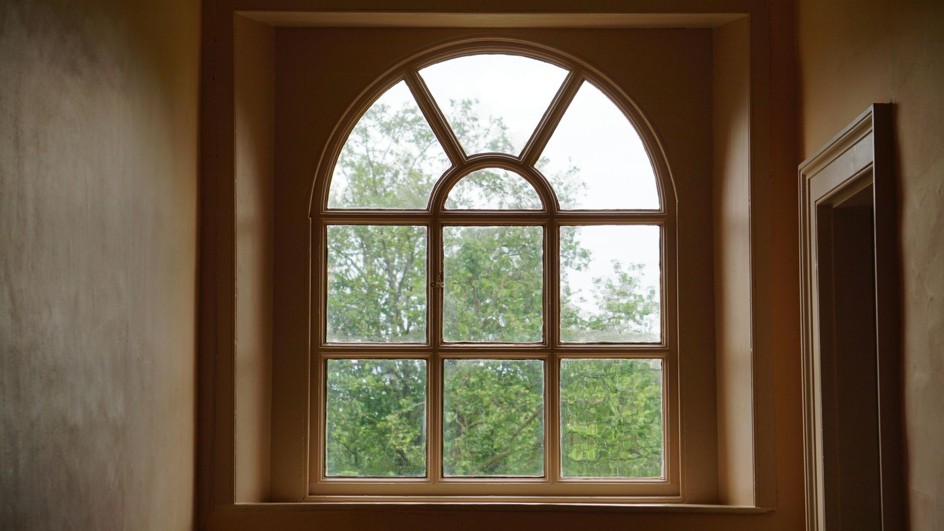 A large arched window with a view of trees in a room.